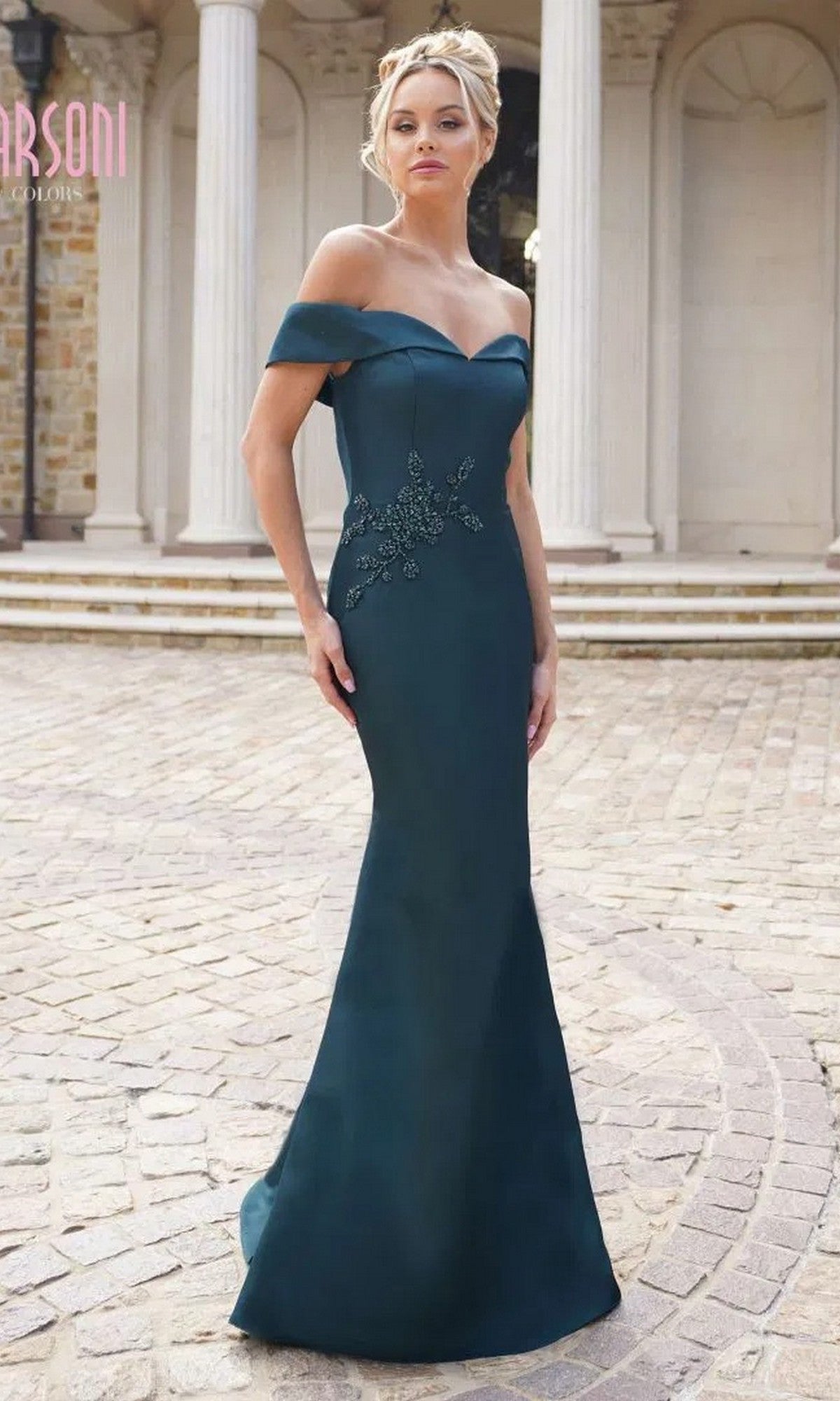 A woman stands outdoors in a deep green Marsoni MV1003 long formal dress, featuring off-the-shoulder satin, beaded floral bodice embellishments, and a fitted floor-length skirt.